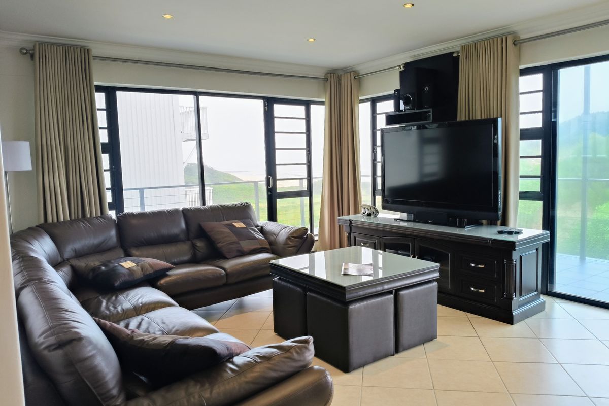 A well-lit living room featuring tiled flooring, recessed downlights, and large aluminium sliding doors that provide ample natural light and access to the balcony.