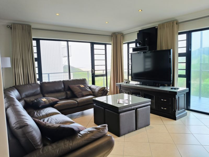 A well-lit living room featuring tiled flooring, recessed downlights, and large aluminium sliding doors that provide ample natural light and access to the balcony.