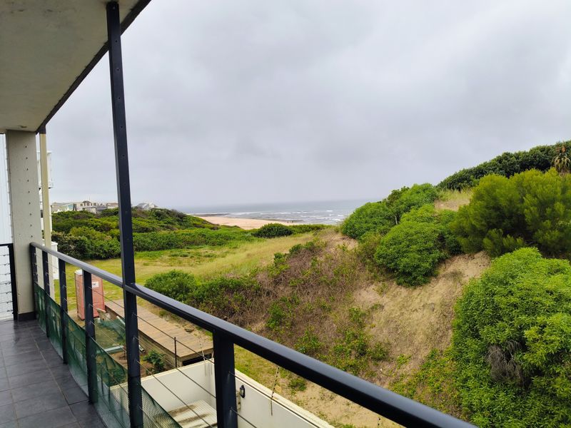 A covered balcony featuring tiled flooring and a metal balustrade, offering scenic views of the surrounding coastal landscape and greenery.