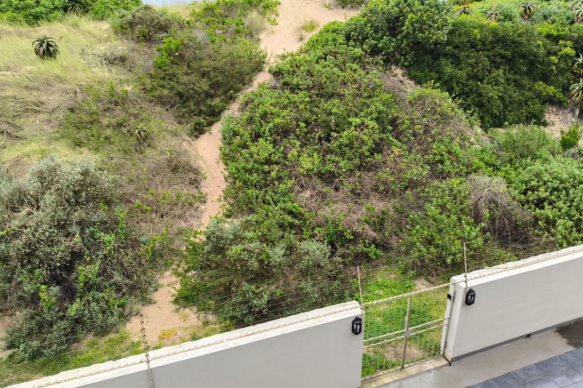 Rear view of the property featuring a tiled patio, secure boundary wall with electric fencing, and direct access to natural coastal dunes.