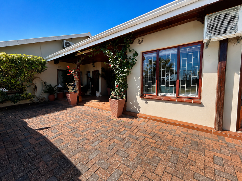 A covered patio area featuring brick paving, timber-framed windows with security bars, and an exterior-mounted air conditioning unit.