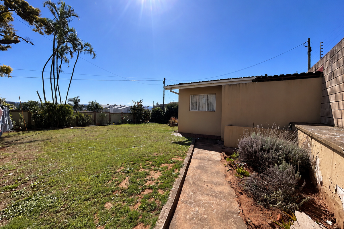 Rear garden area featuring a lawn, concrete pathway, and exterior wall with visible signs of wear and weathering.