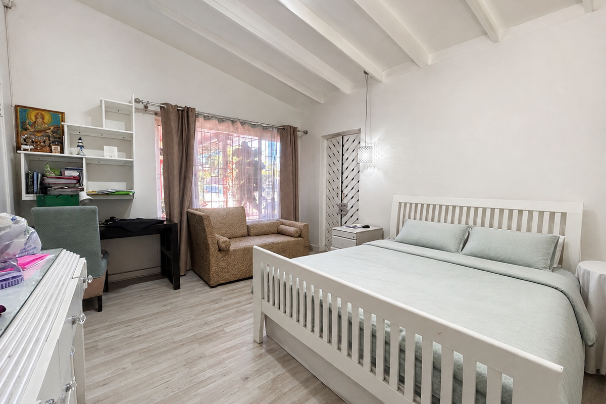 A bright bedroom featuring a vaulted ceiling with exposed beams, light-toned laminate flooring, and a built-in shelving unit.