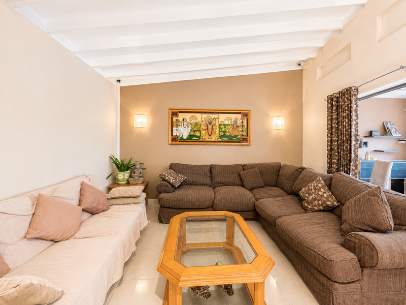 A comfortable living room featuring a high exposed beam ceiling, neutral wall tones, and tiled flooring, creating a bright and inviting space.
