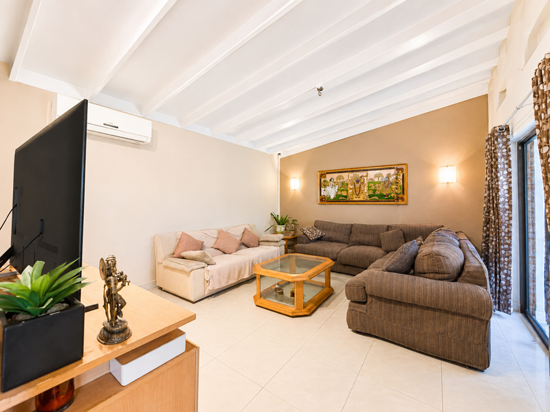 A spacious living room featuring a high exposed beam ceiling, tiled flooring, and a split-system air conditioner, with direct access to an outdoor area.