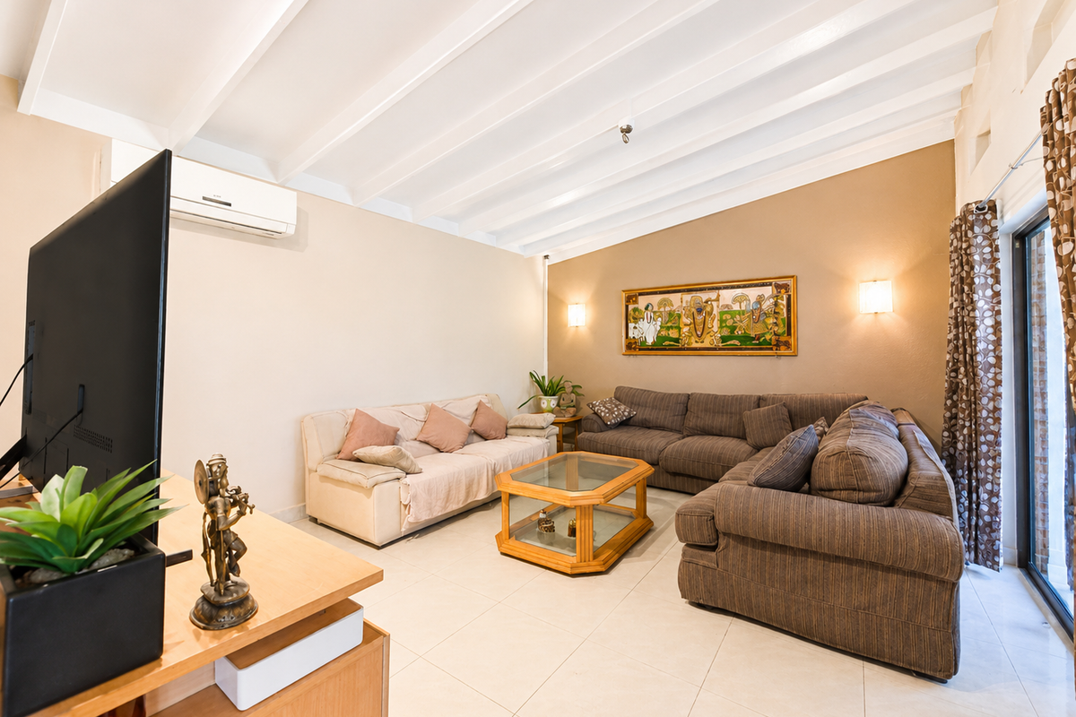A spacious living room featuring a high exposed beam ceiling, tiled flooring, and a split-system air conditioner, with direct access to an outdoor area.