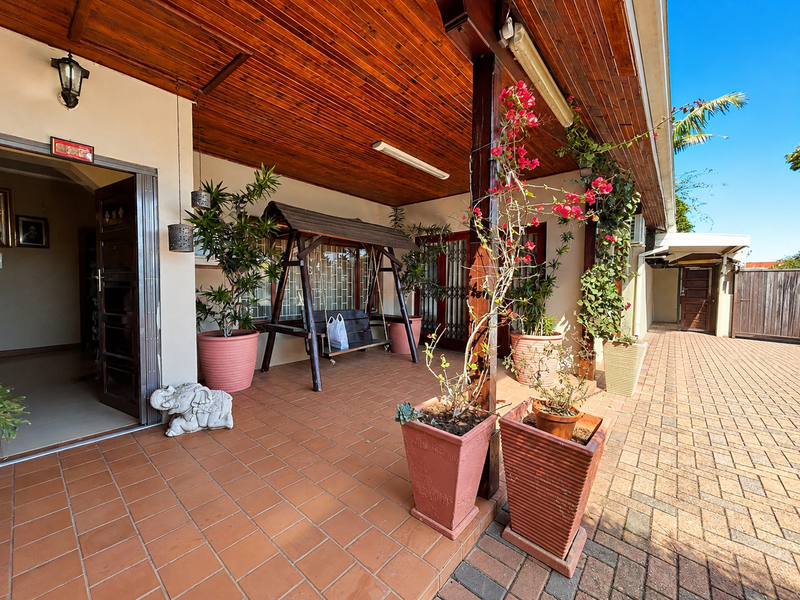 A covered patio area featuring a timber ceiling, terracotta tiling, and direct access to the main entrance and paved driveway.