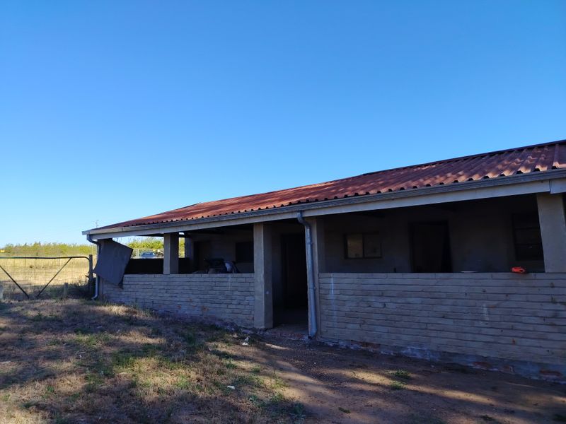 Exterior view of a farm outbuilding featuring a corrugated metal roof and brick masonry construction, showing signs of wear and structural maintenance requirements.