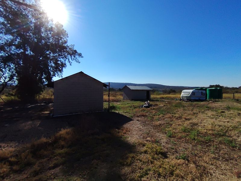Expansive farm land featuring two small outbuildings and water storage tanks under a clear sky.