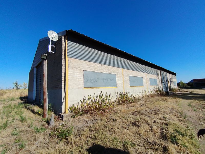 Exterior view of a large agricultural outbuilding featuring brick walls, corrugated metal roofing, and a metal roller shutter door on a rural property.