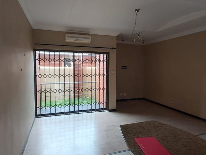 Spacious, empty living area featuring tiled floors, coved ceilings, an air conditioning unit, and a sliding glass door with a security gate.