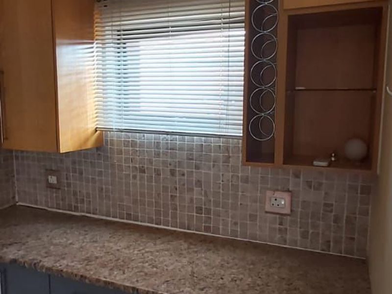 A functional kitchen area featuring granite countertops, mosaic tile backsplash, and modern grey and wood-tone cabinetry with integrated wine storage.