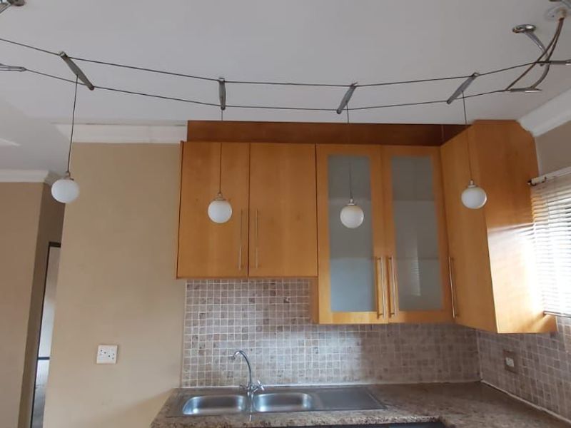 A functional kitchen area featuring wooden cabinetry, granite countertops, a mosaic tile backsplash, and integrated track lighting.