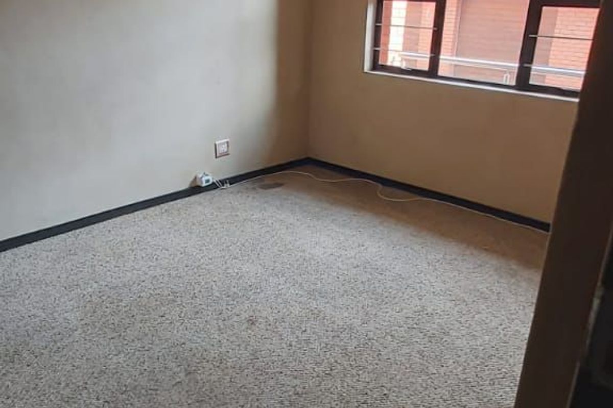 An empty bedroom featuring carpeted flooring, a window with security bars, and a ceiling-mounted light fixture.