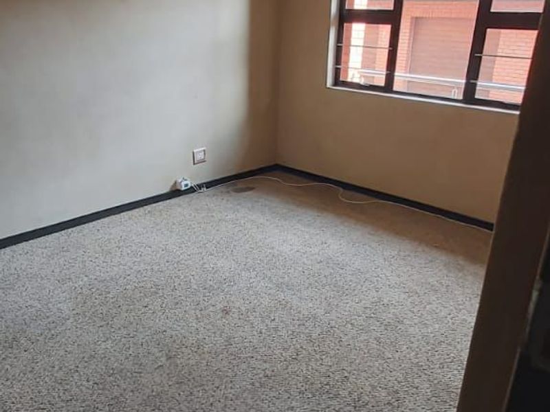 An empty bedroom featuring carpeted flooring, a window with security bars, and a ceiling-mounted light fixture.