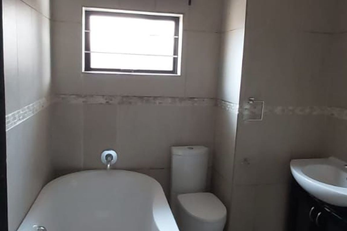A clean, neutral-toned bathroom featuring a modern freestanding bathtub, a wall-mounted toilet, and a vanity unit with a basin.
