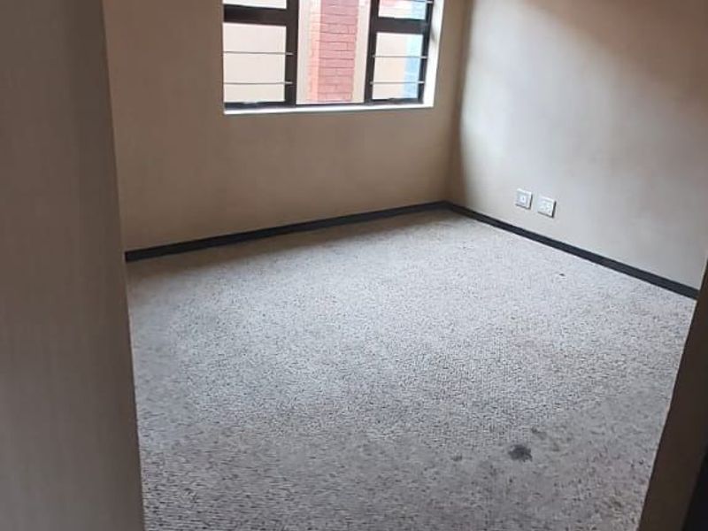 An empty bedroom featuring carpeted flooring and a window with security bars, presenting a blank canvas for potential updates.