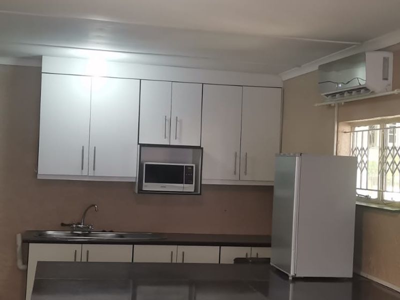 A functional kitchen area featuring white cabinetry, dark tiled breakfast bar, built-in microwave, and a wall-mounted air conditioning unit.