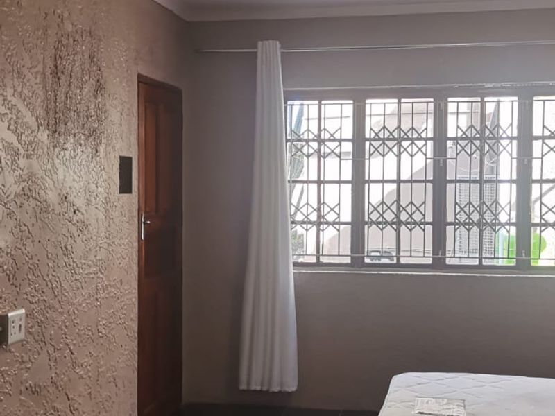 A simple bedroom featuring tiled flooring, textured wall finishes, and a window fitted with a security gate.