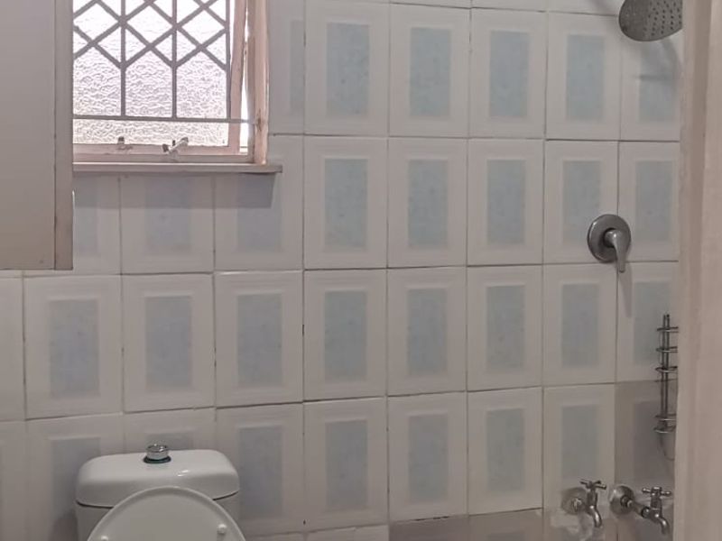 A functional bathroom featuring a pedestal basin, toilet, and bathtub with shower attachment, finished with dated wall tiling and dark floor tiles.