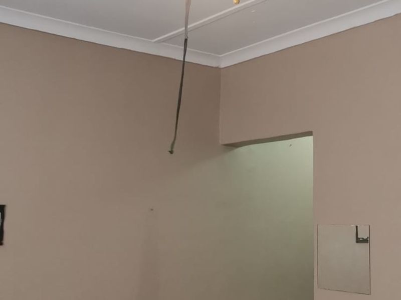 A simple bedroom space featuring a ceiling fan with exposed wiring and tiled flooring, presenting an opportunity for cosmetic updates.
