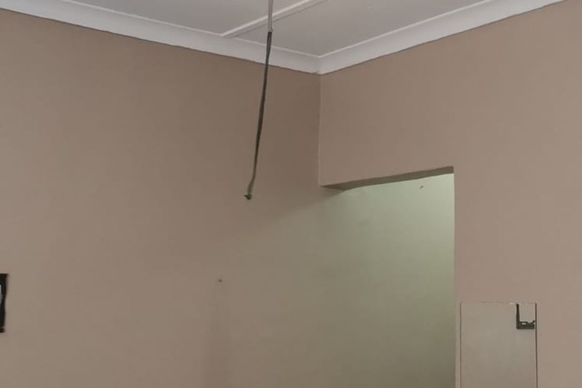 A simple bedroom space featuring a ceiling fan with exposed wiring and tiled flooring, presenting an opportunity for cosmetic updates.