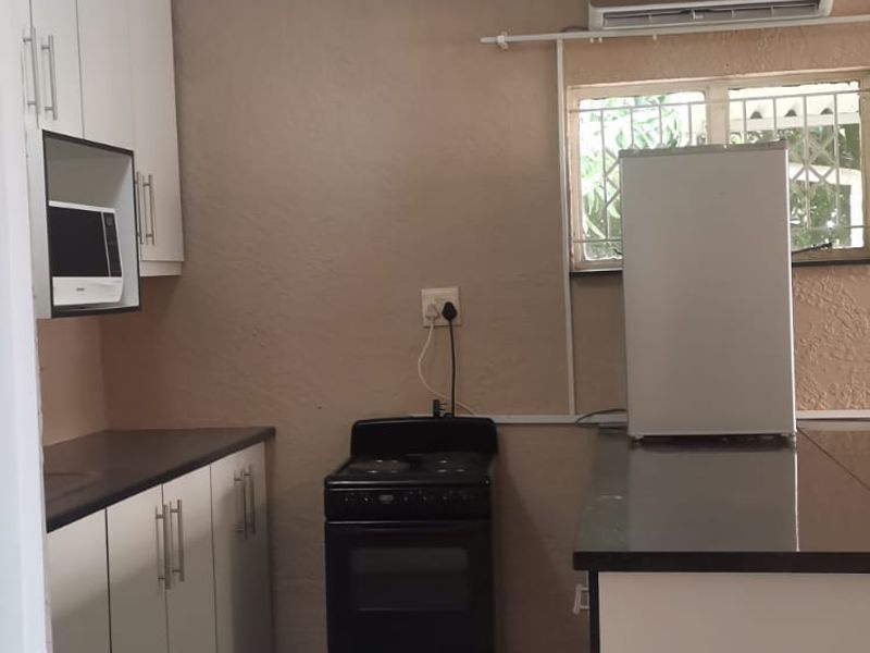 Compact kitchen featuring white cabinetry, black stone countertops, a freestanding stove, and a wall-mounted air conditioning unit.