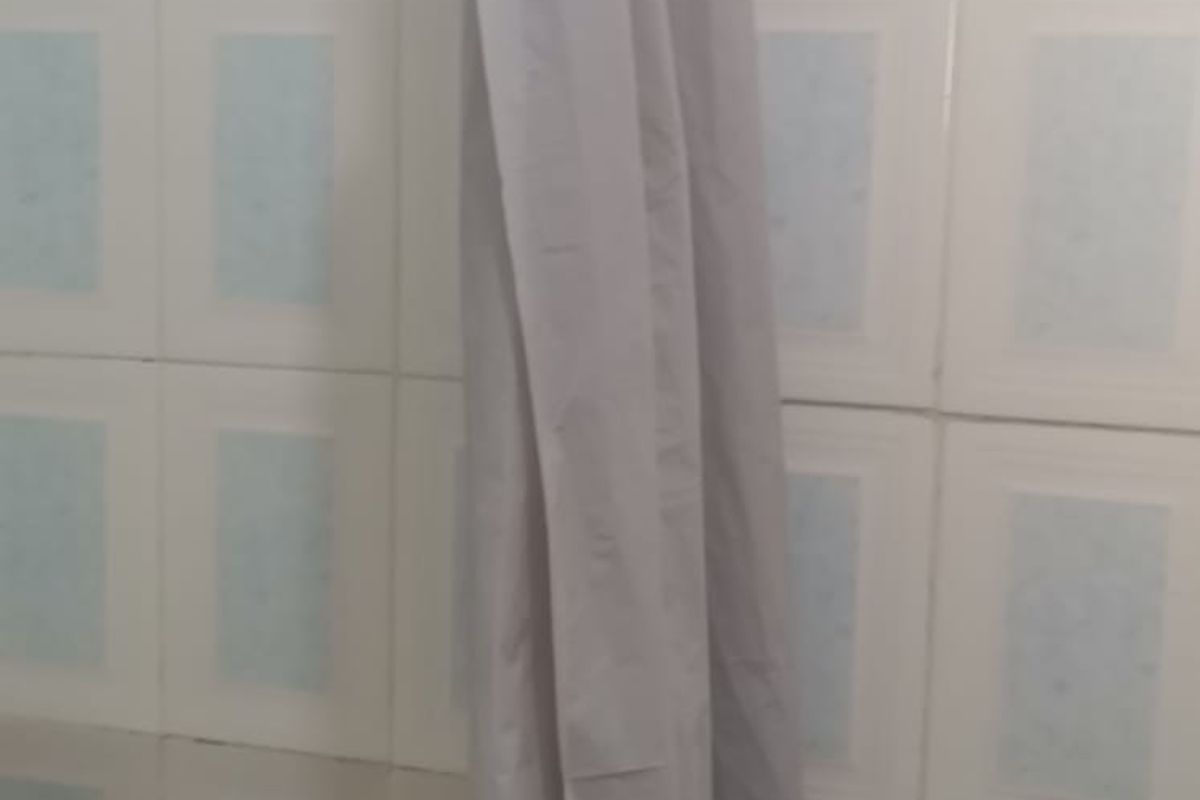 A close-up view of a bathroom shower area featuring dated ceramic wall tiles and a shower curtain.