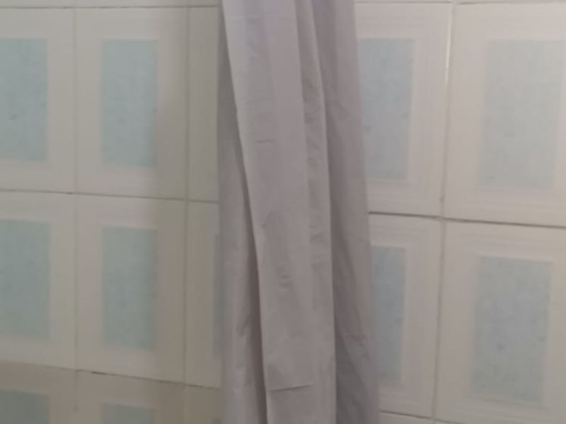 A close-up view of a bathroom shower area featuring dated ceramic wall tiles and a shower curtain.