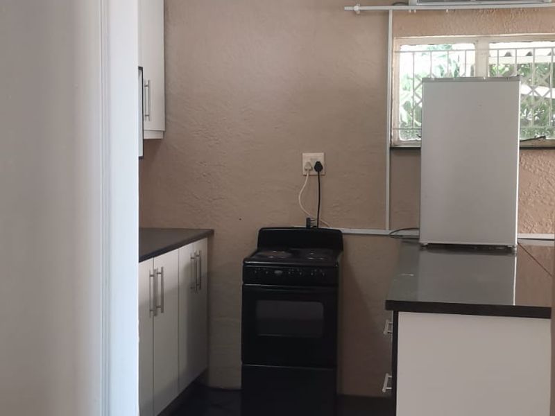 A functional kitchen featuring white cabinetry, black countertops, tiled flooring, and a built-in air conditioning unit.