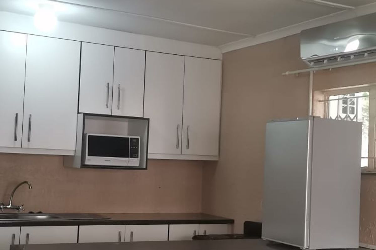 A functional kitchen featuring white cabinetry, dark granite countertops, a tiled breakfast bar, and a wall-mounted air conditioning unit.