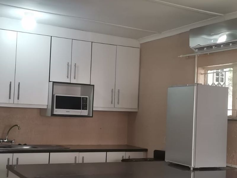 A functional kitchen featuring white cabinetry, dark granite countertops, a tiled breakfast bar, and a wall-mounted air conditioning unit.