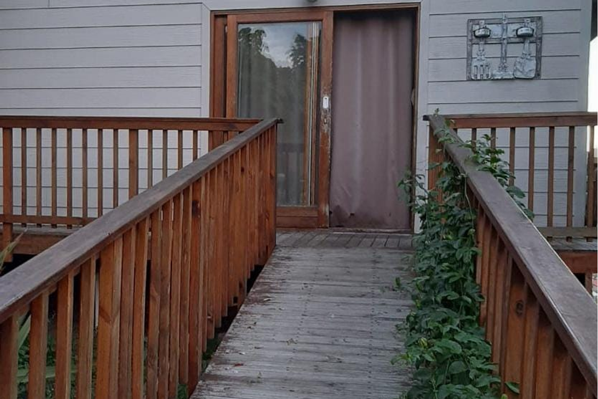 A rear exterior view featuring a timber deck walkway with balustrades leading to a sliding glass door entrance on a weatherboard-clad home.
