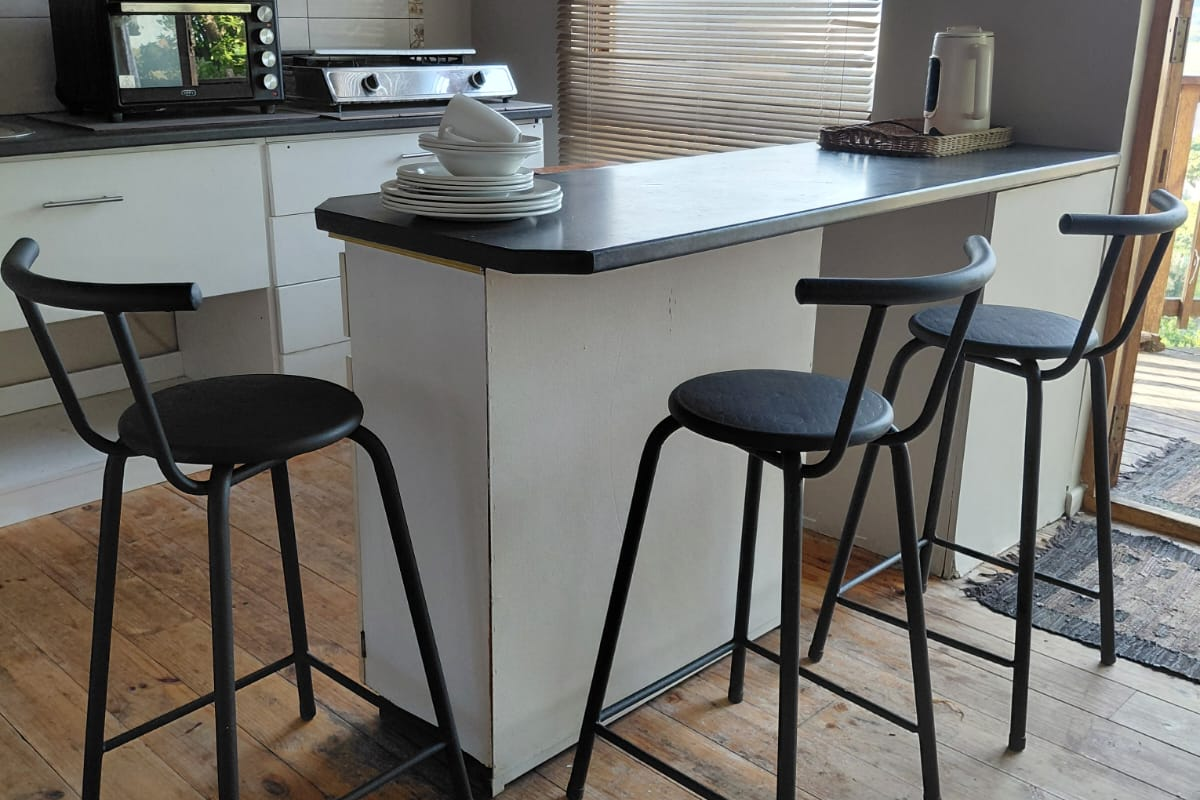 A compact kitchen featuring a breakfast bar, timber flooring, and an arched window, offering a functional layout with potential for modern updates.