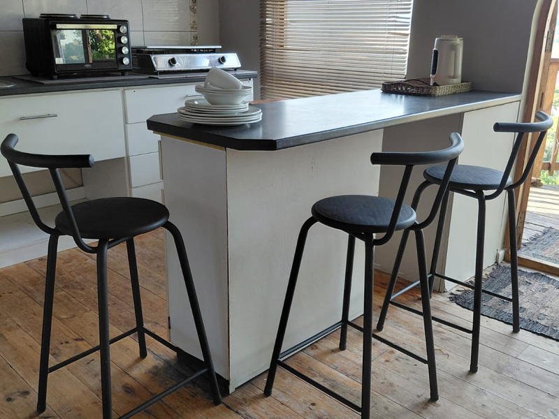 A compact kitchen featuring a breakfast bar, timber flooring, and an arched window, offering a functional layout with potential for modern updates.