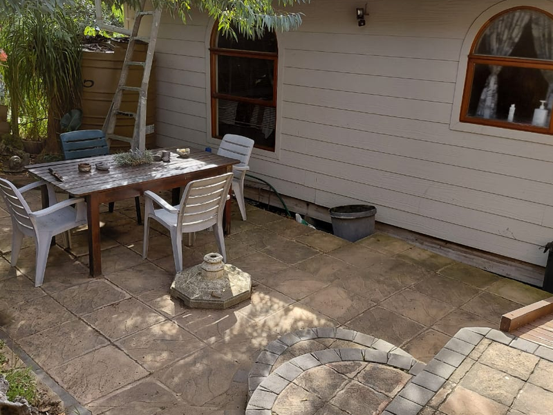 A paved outdoor patio area featuring arched windows, corrugated metal roofing, and brick-edged steps, providing a functional space for outdoor living.