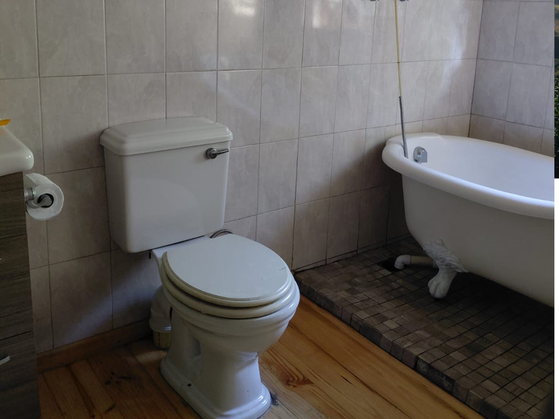 A bathroom featuring a classic clawfoot bathtub, toilet, and a mix of timber and mosaic tile flooring with wall-to-wall tiling.
