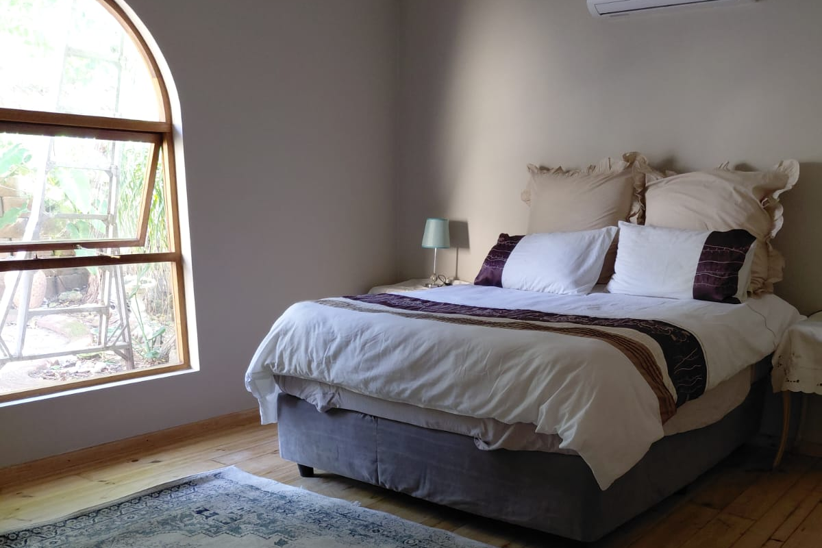 A well-lit bedroom featuring polished timber flooring, a distinctive arched window, and a wall-mounted split-system air conditioning unit.