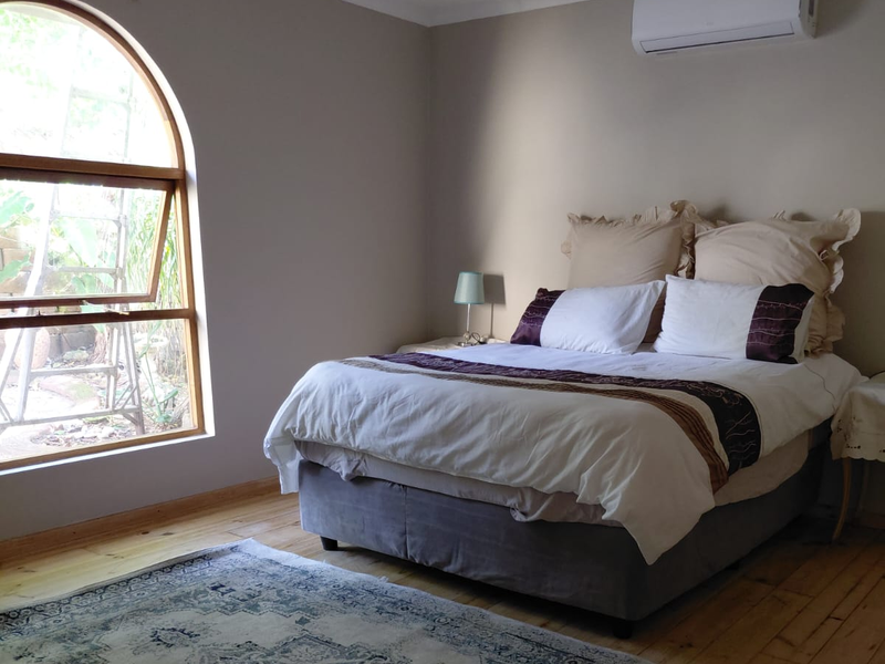 A well-lit bedroom featuring polished timber flooring, a distinctive arched window, and a wall-mounted split-system air conditioning unit.