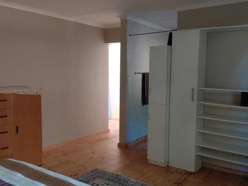 Bedroom featuring timber flooring, built-in shelving units, and a partial tiled wall leading to an adjacent space.