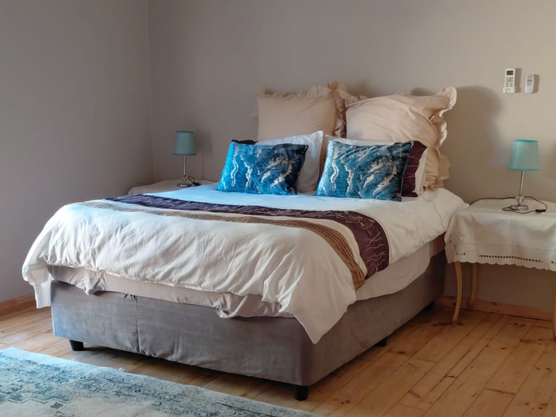 A well-maintained bedroom featuring polished timber flooring, neutral wall tones, and a wall-mounted split-system air conditioning unit.