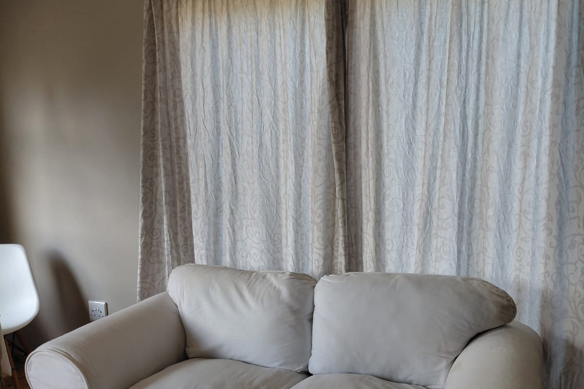 A living room area featuring neutral wall tones and floor-to-ceiling curtains, providing a simple and functional space.