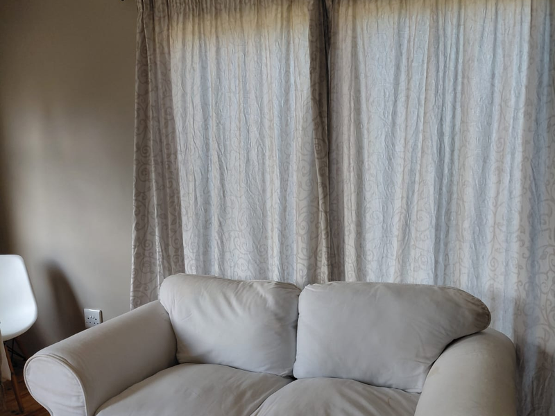 A living room area featuring neutral wall tones and floor-to-ceiling curtains, providing a simple and functional space.