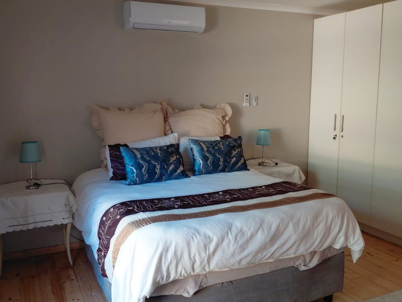 A well-maintained bedroom featuring timber flooring, a built-in wardrobe, and a wall-mounted split-system air conditioner for climate control.