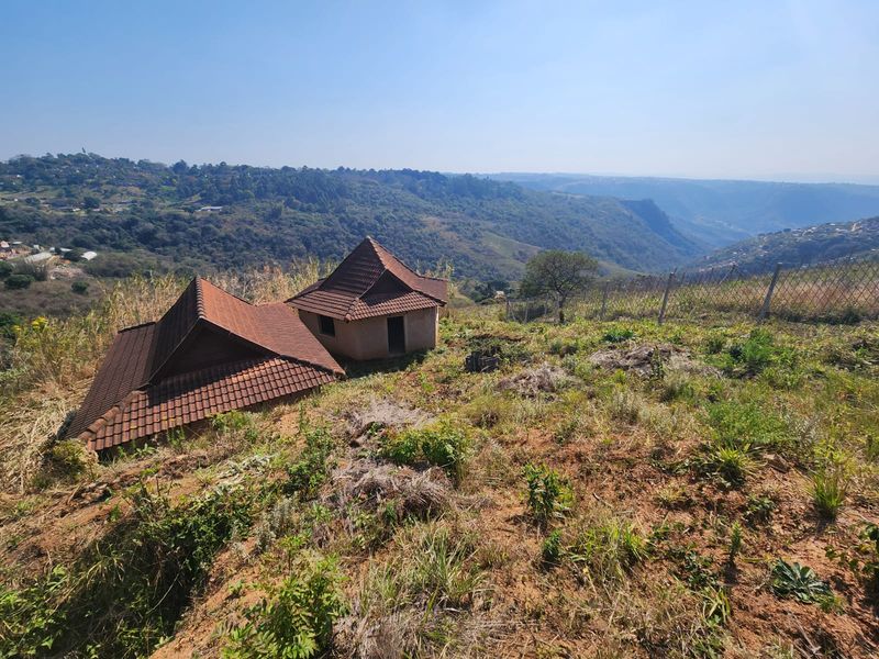 Elevated view of a property featuring two small structures with tiled roofs, set against a scenic valley landscape with wire fencing.