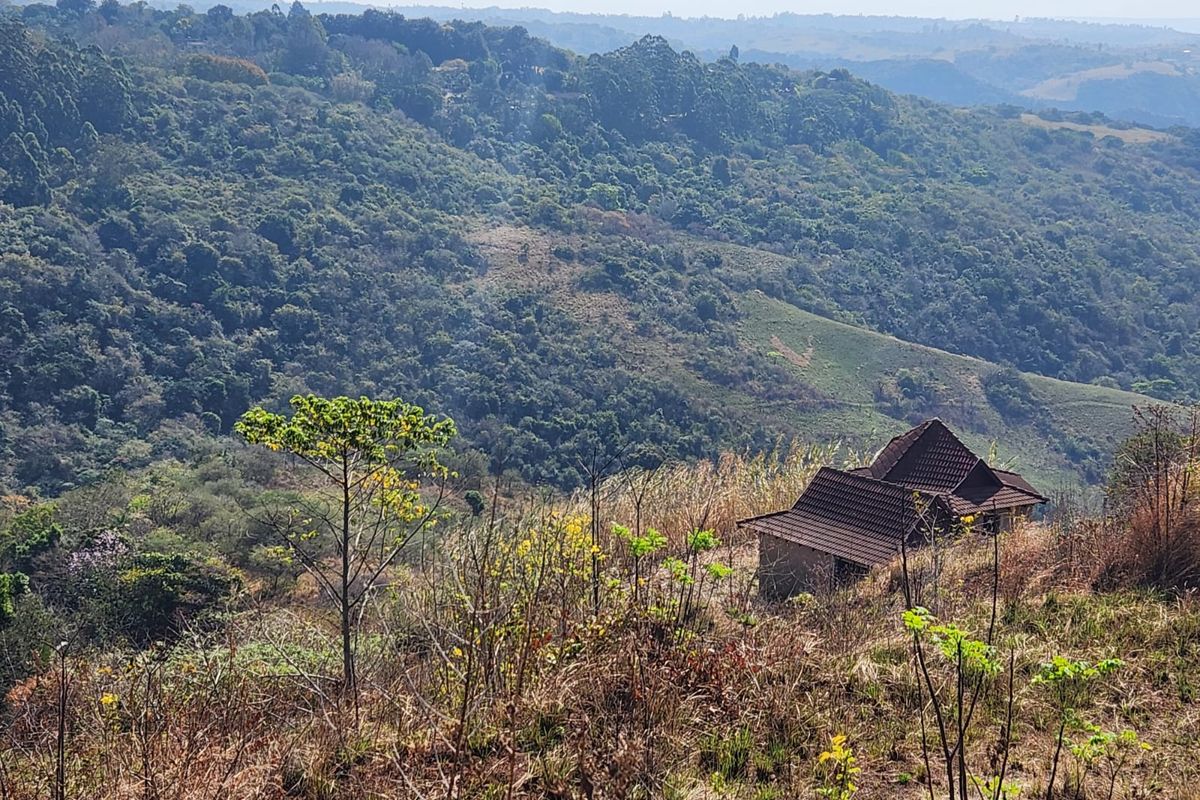 A scenic elevated view overlooking a lush, hilly landscape with a small residential structure featuring a tiled roof nestled in the terrain.