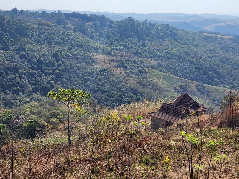 A scenic elevated view overlooking a lush, hilly landscape with a small residential structure featuring a tiled roof nestled in the terrain.