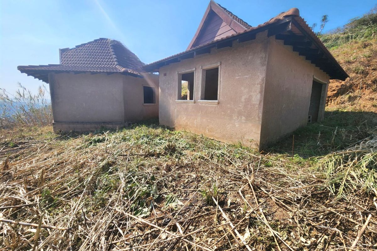 Exterior view of an unfinished residential structure featuring tiled roofing and plastered walls, situated on an undeveloped plot with significant vegetation.