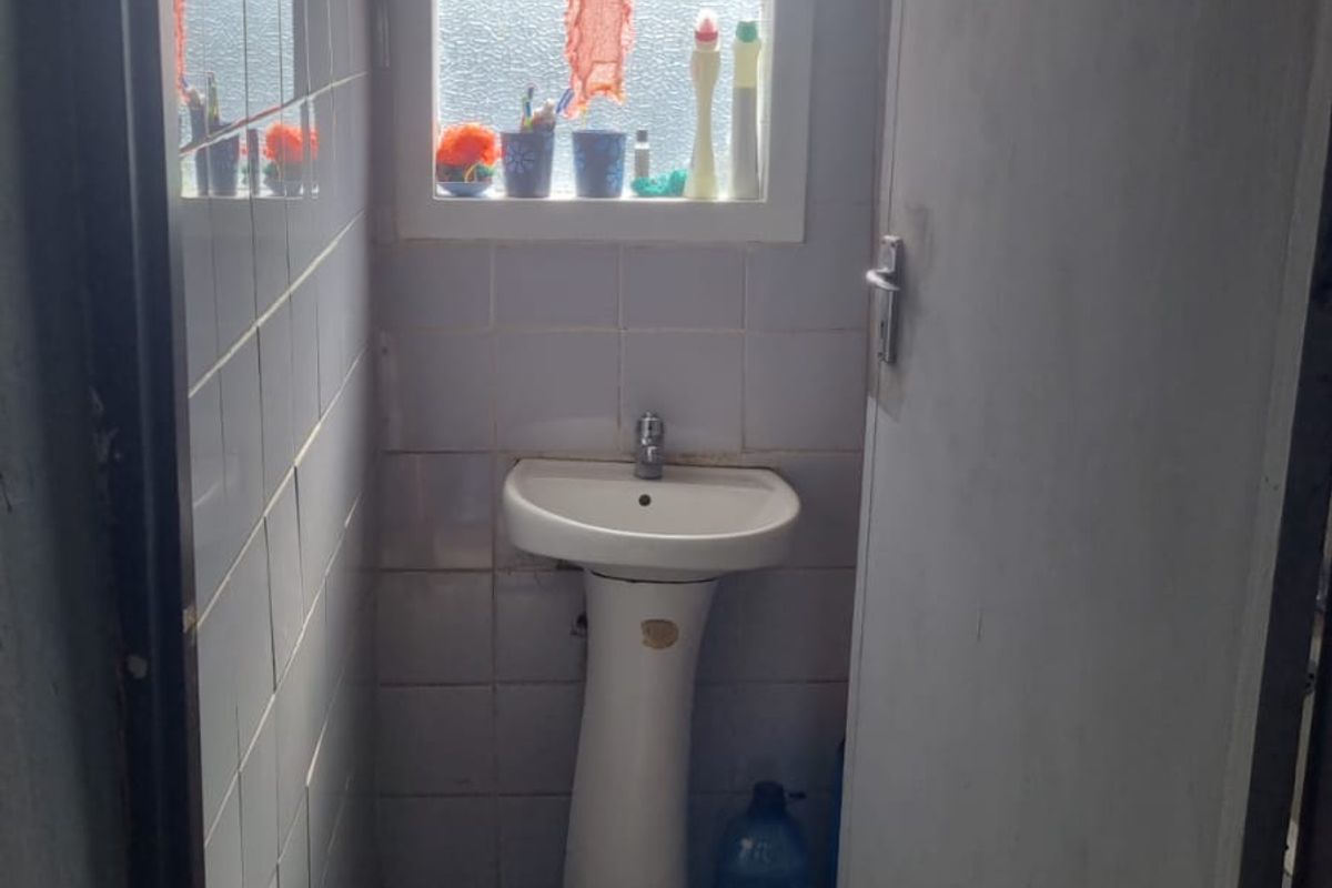 A small, functional bathroom featuring a pedestal basin, tiled walls, and tiled flooring, requiring cosmetic updates to improve its overall condition.