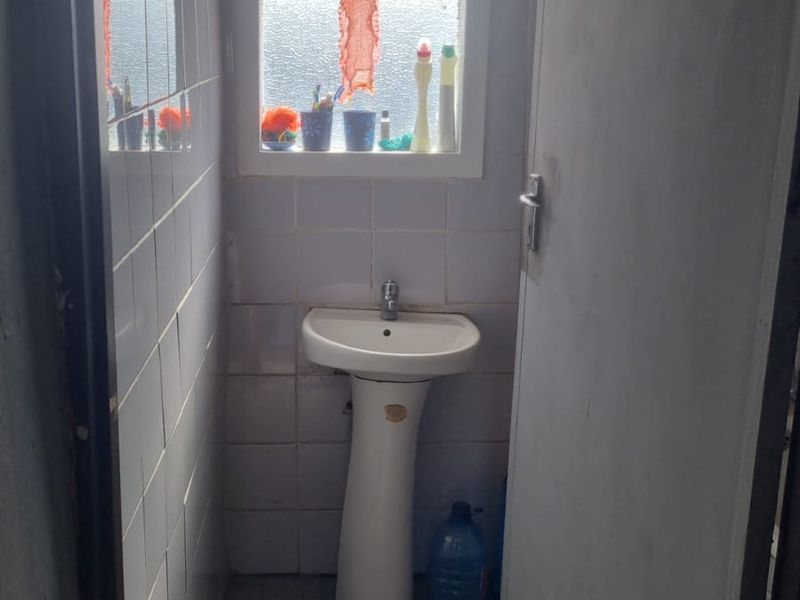 A small, functional bathroom featuring a pedestal basin, tiled walls, and tiled flooring, requiring cosmetic updates to improve its overall condition.